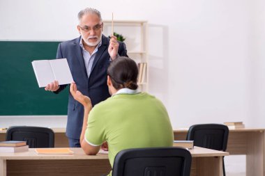 Sınıfta yaşlı öğretmen ve genç erkek öğrenci var.