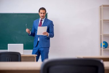 Yeşil panonun önünde takım elbiseli genç bir öğretmen.