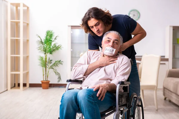 Vieil homme en fauteuil roulant et jeune mauvais soignant à l'intérieur — Photo