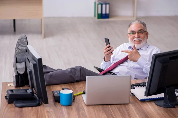 Oude mannelijke baas zit op het bureaublad in het kantoor — Stockfoto