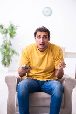 Genç adam evde televizyon izliyor.