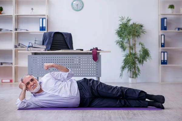 Verouderde mannelijke werknemer doet fysieke oefeningen tijdens de pauze — Stockfoto