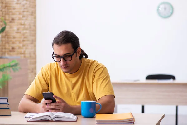 Joven estudiante masculino sosteniendo el teléfono móvil durante la preparación del examen — Foto de Stock