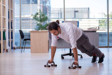 Genç erkek çalışan ofiste spor egzersizleri yapıyor.