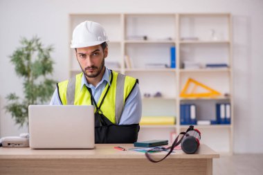 Genç kollu yaralı erkek mimar ofiste çalışıyor.