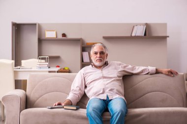 Yaşlı adam evdeki kanepede oturuyor.