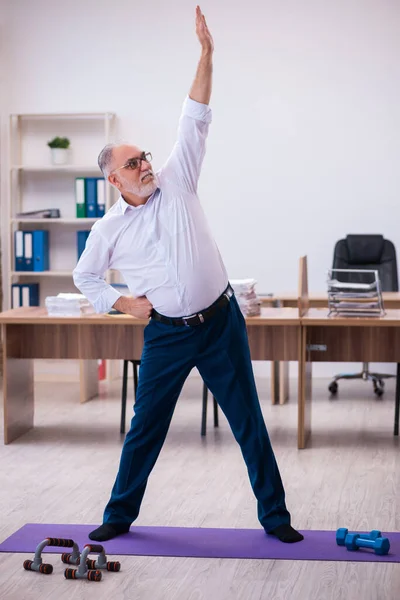 Velho empresário empregado fazendo exercícios esportivos no escritório — Fotografia de Stock