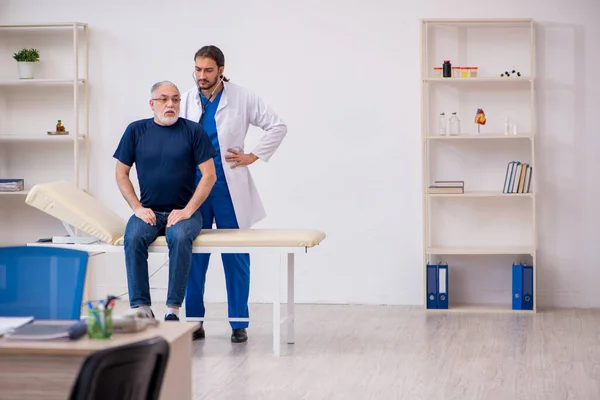 Viejo paciente masculino visitando al joven médico masculino —  Fotos de Stock