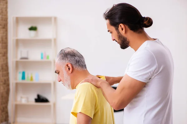 Velho paciente masculino visitando jovem médico chiropractor — Fotografia de Stock