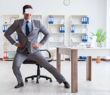 Ofiste egzersiz yapan işadamı VR gözlüğü takıyor.