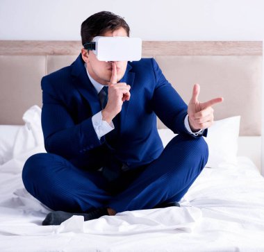 Yatak odasında sanal gerçeklik kulaklığı takan bir iş adamı.