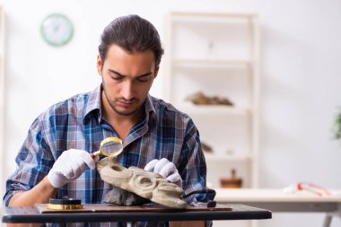 Genç erkek arkeolog eski Afrika taş maskesi üzerinde çalışıyor.