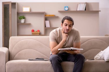 Evde kitap okuyan genç bir erkek öğrenci.