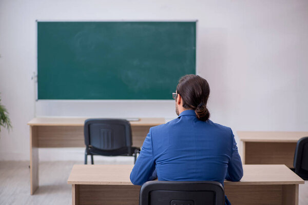 Young male teacher in suit in front of green board