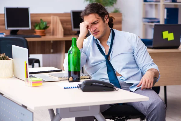 Mladý zaměstnanec pije alkohol na pracovišti — Stock fotografie