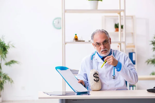 Velho médico masculino segurando saco de dinheiro no hospital — Fotografia de Stock