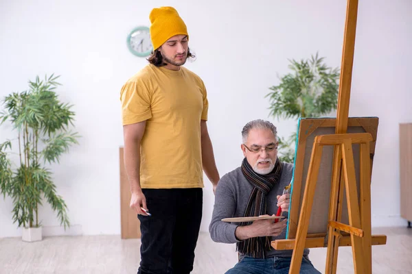 Old man taking lesson from young painter