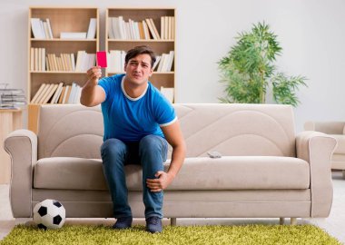 Evdeki kanepede oturup futbol izleyen bir adam.