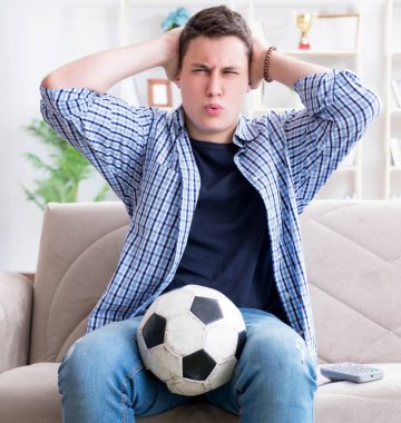 Evde futbol izleyen genç bir öğrenci.