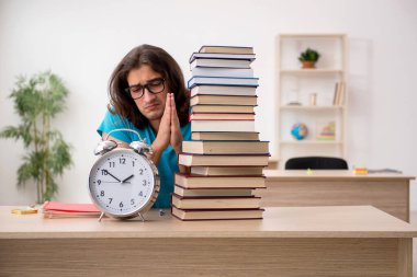 Genç bir erkek öğrenci ve sınıfta bir sürü kitap var.