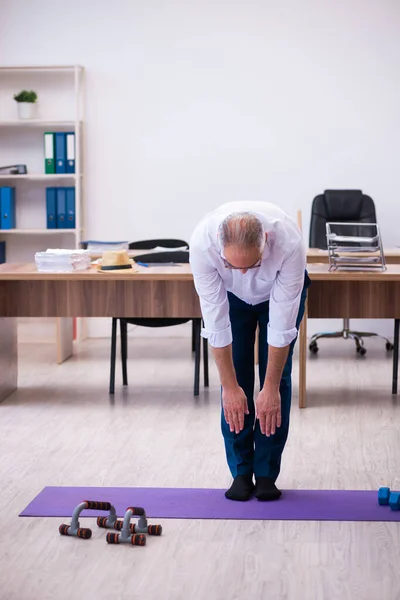 Old businessman employee doing sport exercises in the office