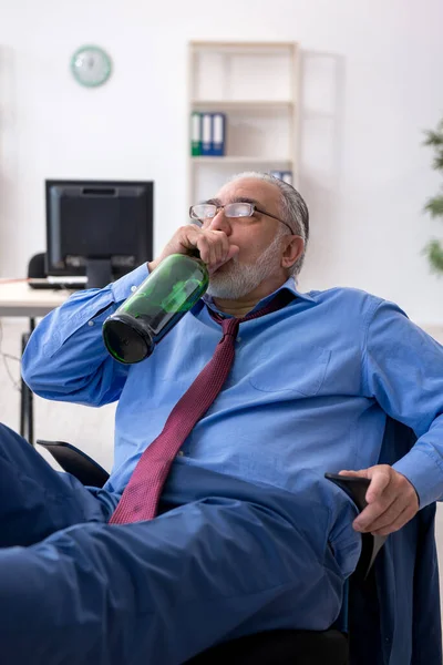 Gammal manlig anställd dricker alkohol på kontoret — Stockfoto