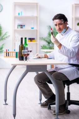 Erkek kimyager laboratuvarda şarap örneklerini inceliyor.