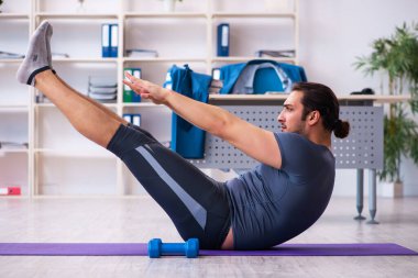 Genç yakışıklı çalışan ofiste spor egzersizleri yapıyor.