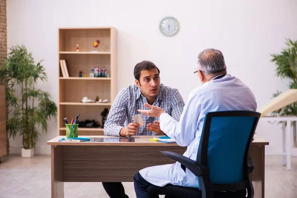 Ung manlig patient besöker äldre manlig läkare — Stockfoto