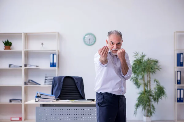 Verouderde mannelijke werknemer doet fysieke oefeningen tijdens de pauze — Stockfoto