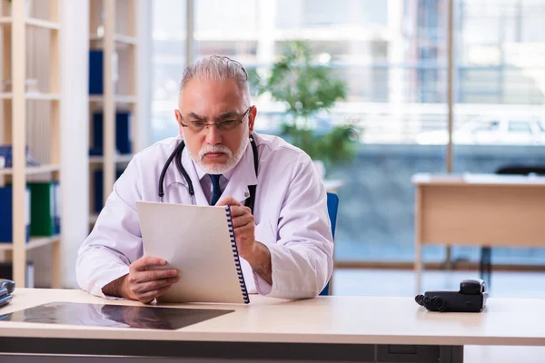 Yaşlı erkek doktor klinikte not alıyor. — Stok fotoğraf