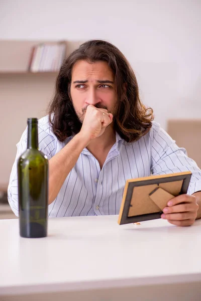Giovane uomo che beve alcol a casa in concetto di amore infelice — Foto Stock