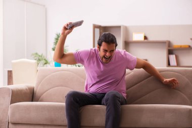 Genç adam salgın sırasında evde televizyon izliyor.