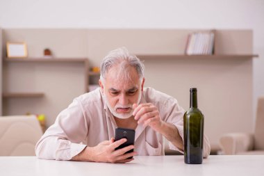 Yaşlı adam evde alkol içiyor.