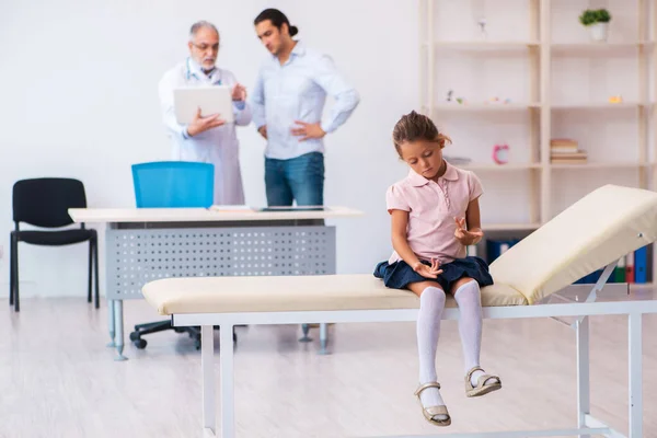Small girl with her father visiting old male doctor — ストック写真