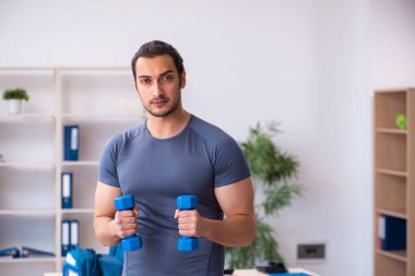 Genç yakışıklı çalışan ofiste spor egzersizleri yapıyor.