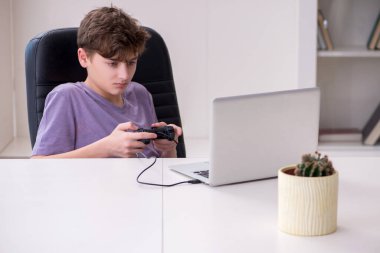 Okullu çocuk evde bilgisayar oyunu oynuyor.