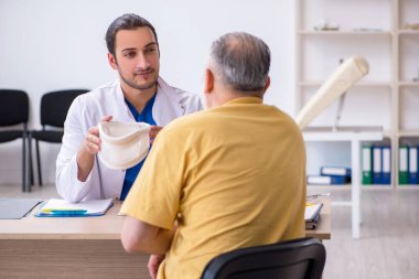 Yaşlı boynu yaralı bir adam genç erkek doktoru ziyaret ediyor.