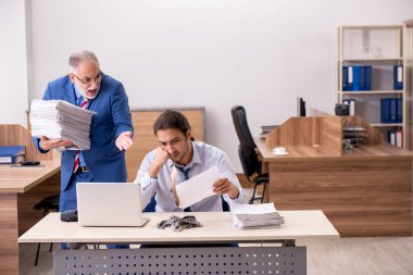 Genç erkek çalışan ve yaşlı patron iş yerinde kağıtları yakıyor.