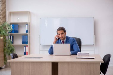 Genç erkek çalışan ofiste beyaz tahtanın önünde oturuyor.