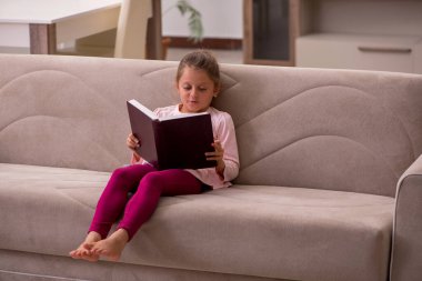 Evde kitap okuyan küçük bir kız.