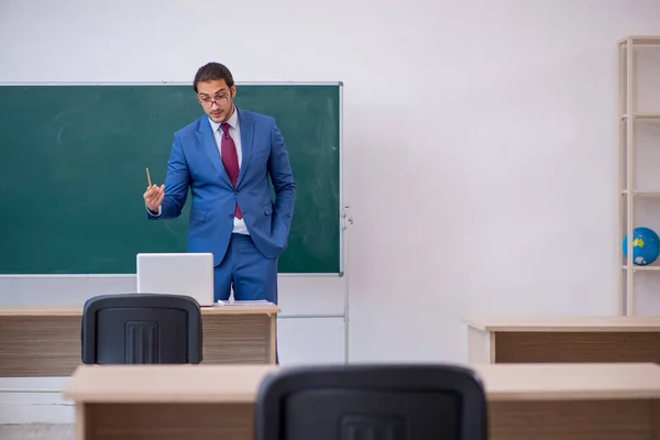 Young male teacher in suit in front of green board