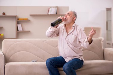 Yaşlı adam evde alkol içiyor.