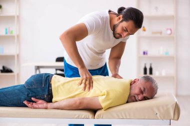 Yaşlı erkek hasta, genç erkek doktor masörünü ziyaret ediyor.