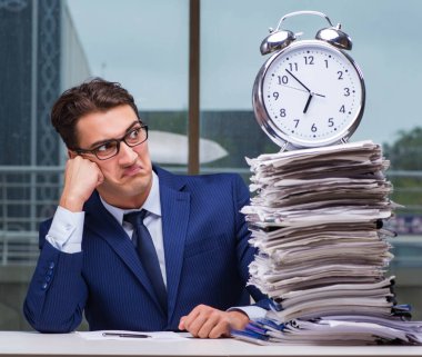 Yığınla evrak işi ve alarm sistemi olan bir iş adamı.