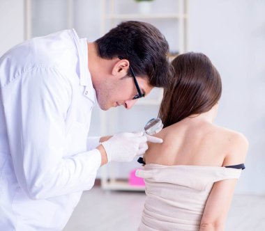 Doktor kadın hastanın derisini muayene ediyor.