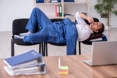 Genç bir erkek çalışan ofiste koltuklarda uyuyor.