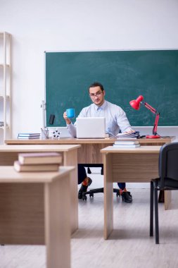 Genç erkek öğretmen yeşil panonun önünde.