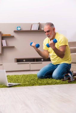 Yaşlı adam evde spor egzersizleri yapıyor.