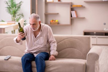Yaşlı adam evde alkol içiyor.
